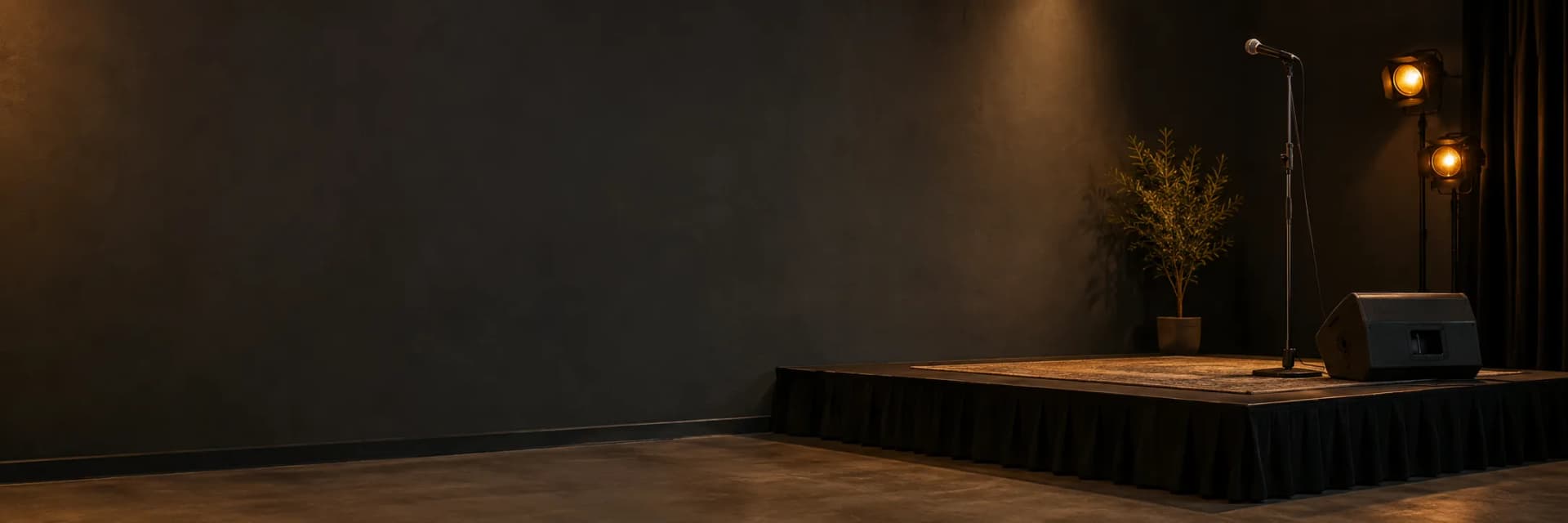 A small stage with a microphone stand, a speaker and two warm spotlights in a dark room