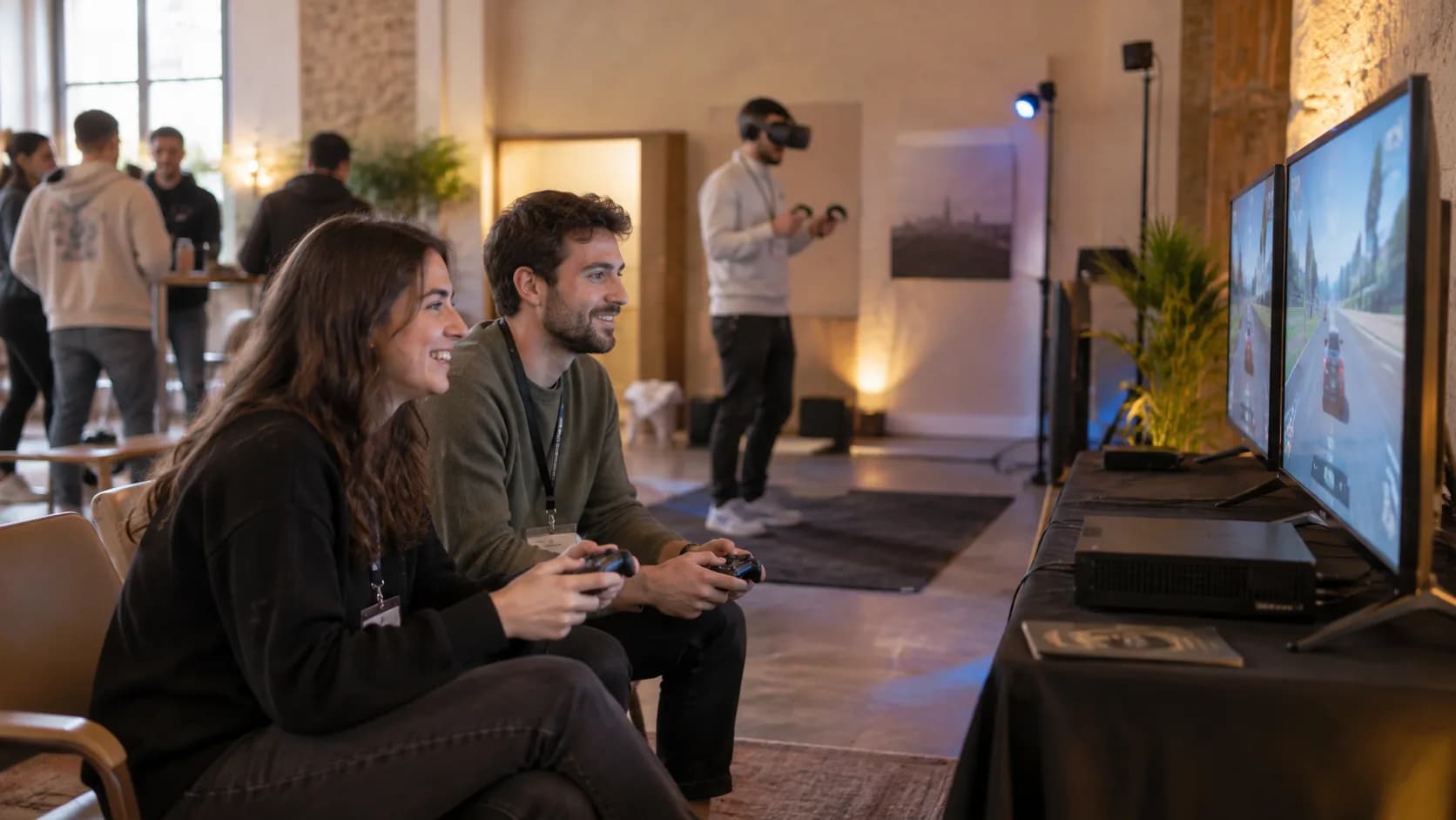 Dos participantes juegan con mandos ante pantallas y otra persona utiliza un visor de realidad virtual