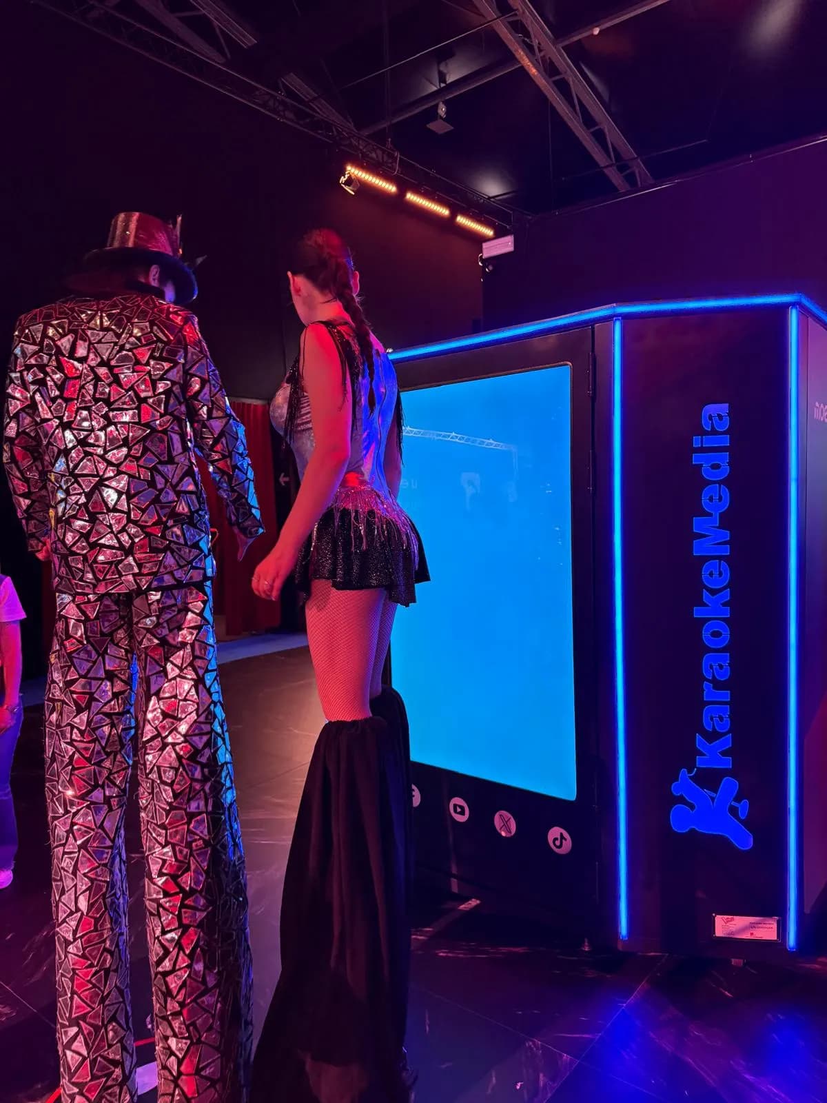 Dos artistes amb xanques d'esquena, mirant la cabina de karaoke amb la pantalla de Moeve