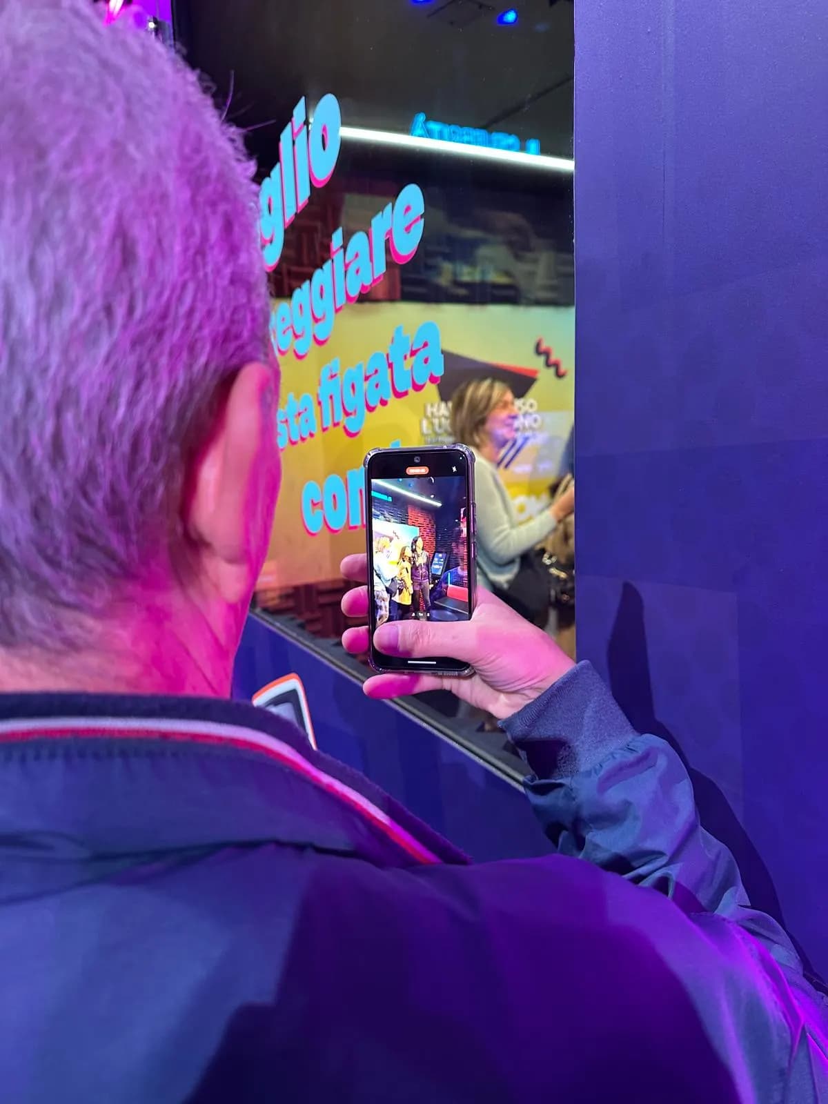 Guest seen from behind filming the performance inside the karaoke booth on a phone