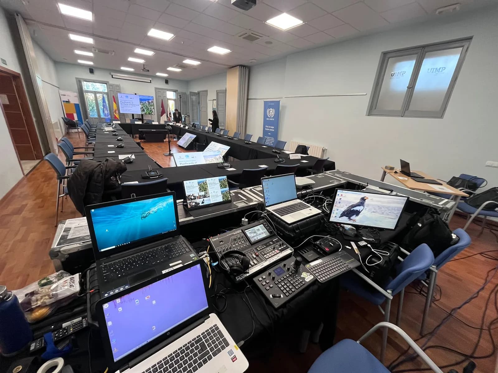 Technical control desk in the foreground and, behind it, the UIMP room in Cuenca with the U-shaped table, the conference units and the main screen before the start