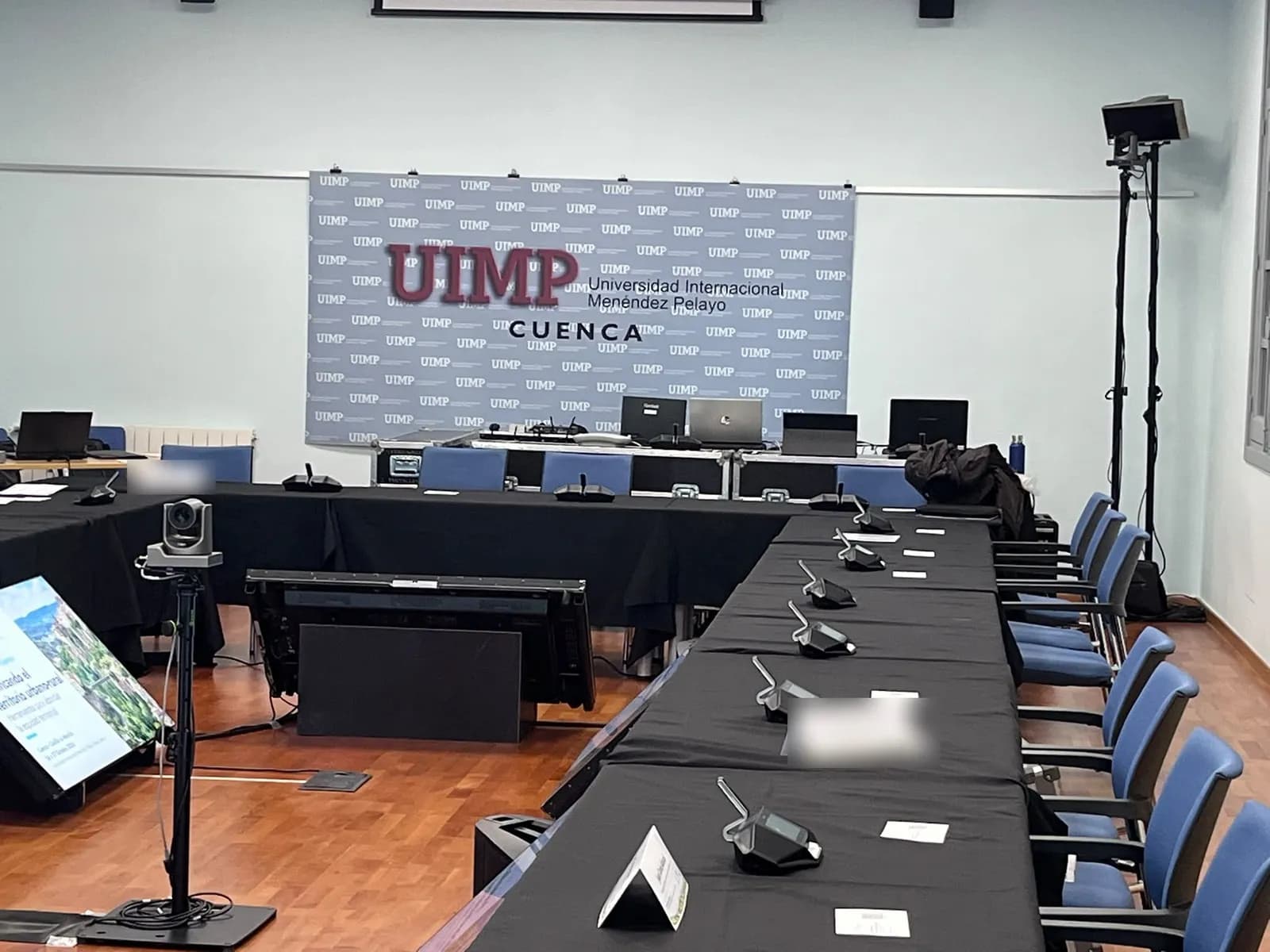 UIMP room in Cuenca with conference units at each seat at the table, a robotic camera on a tripod and a tilted monitor inside the U